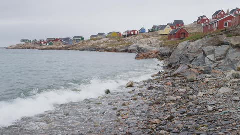 Water crashes against a rocky coastline near a village