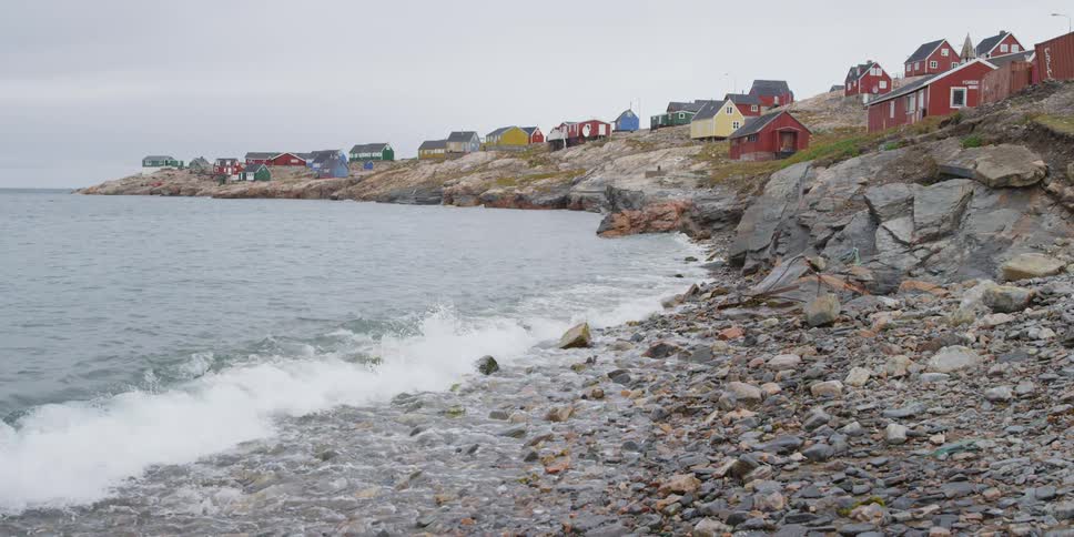 Water crashes against a rocky coastline near a village