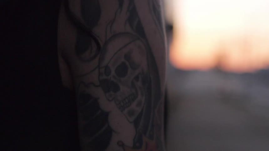 The tattooed arm of a person standing outside at sunset