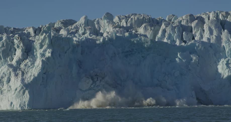 Snow and ice fall from the side of a mountain and collapse into a large body of water