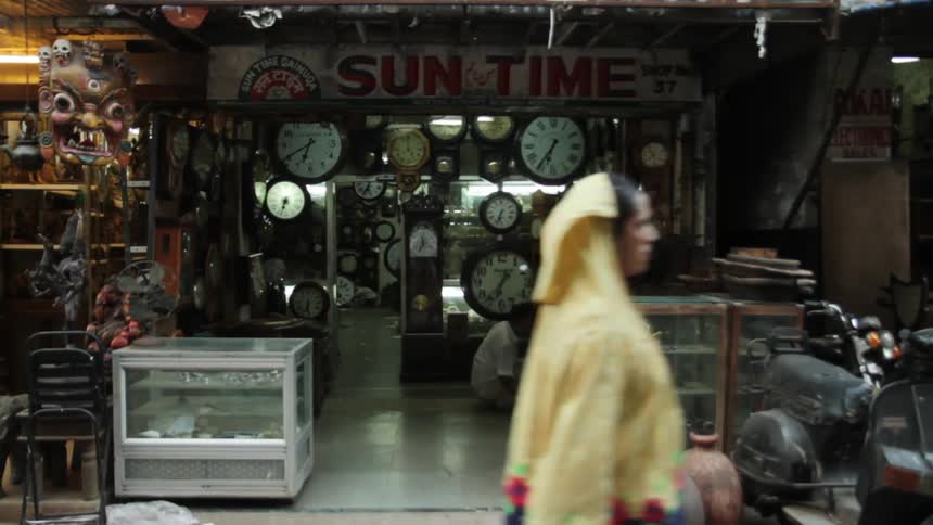 A man is squatting while cleaning the floor of a timepiece store while pedestrians walk by