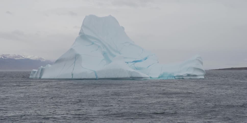 An iceberg in the sea with snow-capped mountains in the background