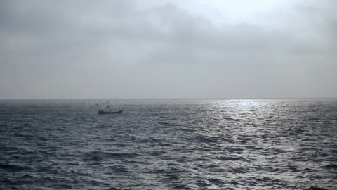 A small boat drifts alone in the ocean on a cloudy day