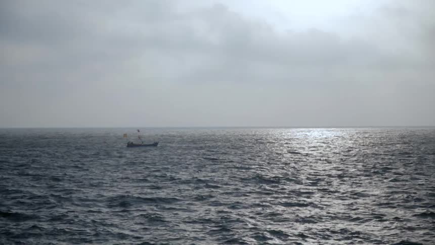 A small boat drifts alone in the ocean on a cloudy day