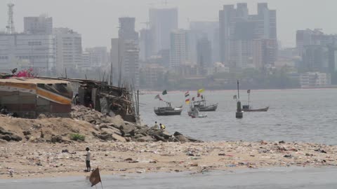 Boats still by the shore as people walk across the rocks on a cloudy day