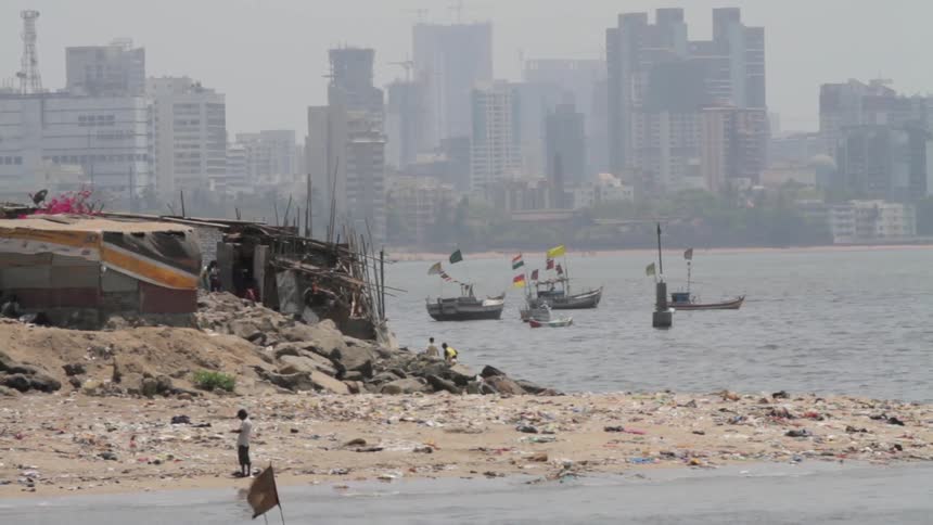 Boats still by the shore as people walk across the rocks on a cloudy day