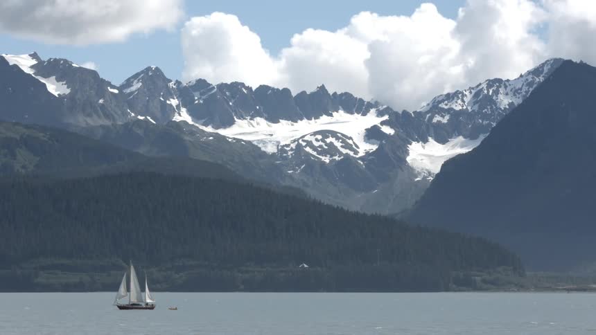 A sailboat is on a lake near a snow covered mountain