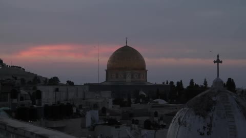 The sun sets behind a domed building