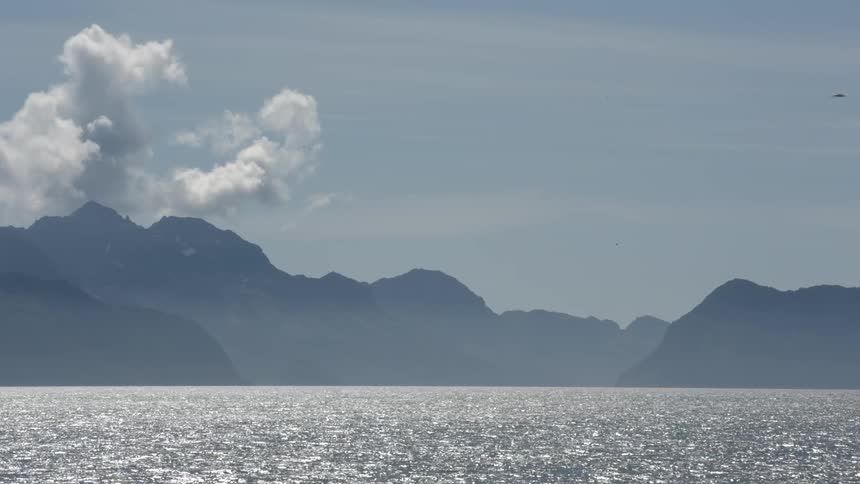 Clouds hover over the mountains while a body of water flows in the foreground