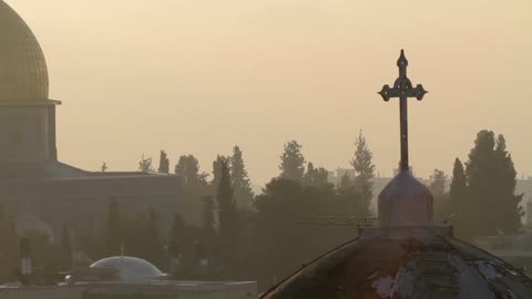 A cross stands silhouetted against an amber sky