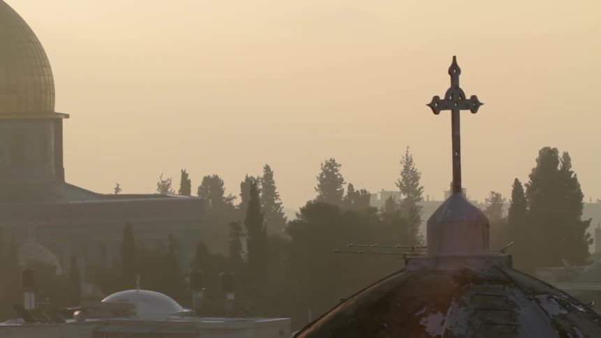 A cross stands silhouetted against an amber sky