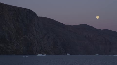 A rocky mountain sitting on an arctic body of water during nightfall