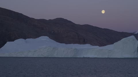 A giant glacier seen in the foreground while the moon is in the background