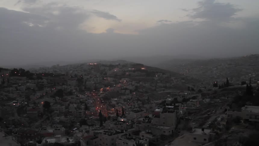 Lights start to come on in houses in a dense neighborhood as dusk turns to evening