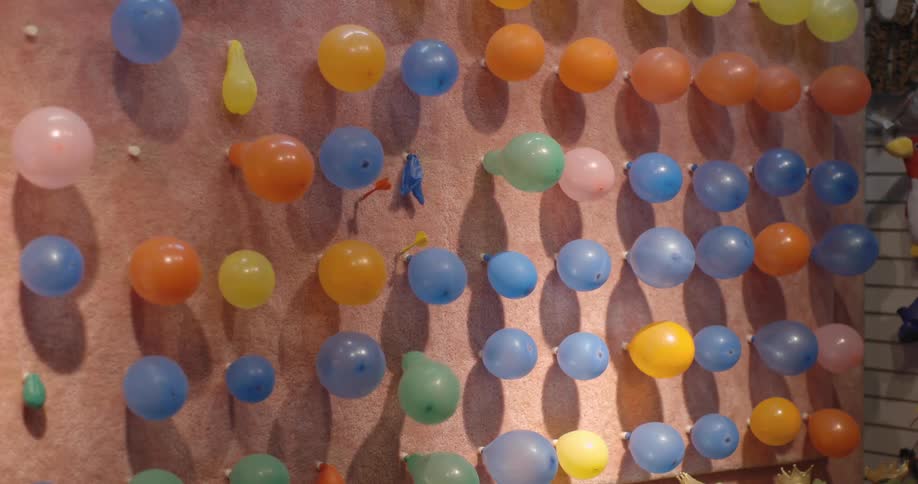 Darts are thrown at a wall of balloons