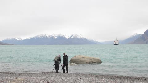 Two men taking pictures of a ship at sea from the shore