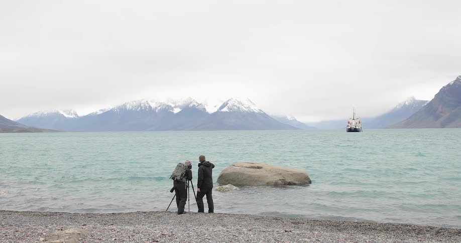 Two men taking pictures of a ship at sea from the shore