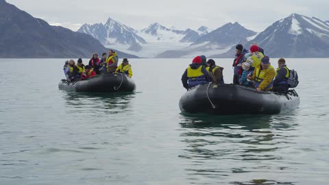 Inflatable boats full of people near snow covered mountains