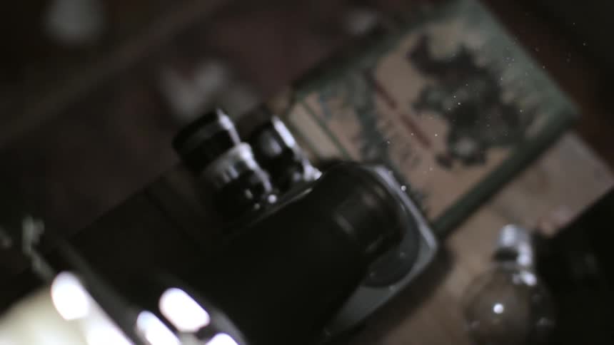 A projector glows as small white particles float down in the light above a bulb and a book
