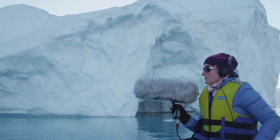 A woman holds a microphone near a glacier