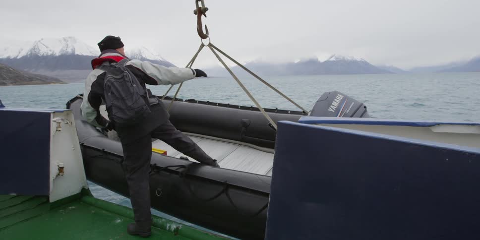 A raft is lowered into the ocean and a man climbs aboard