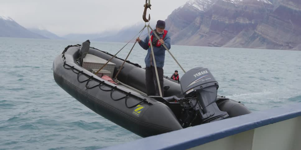 A man stands on an inflatable boat as it is lowered into the ocean