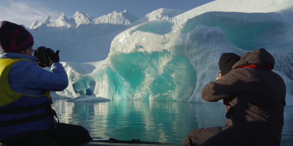 People taking photographs of an iceberg on a clear day