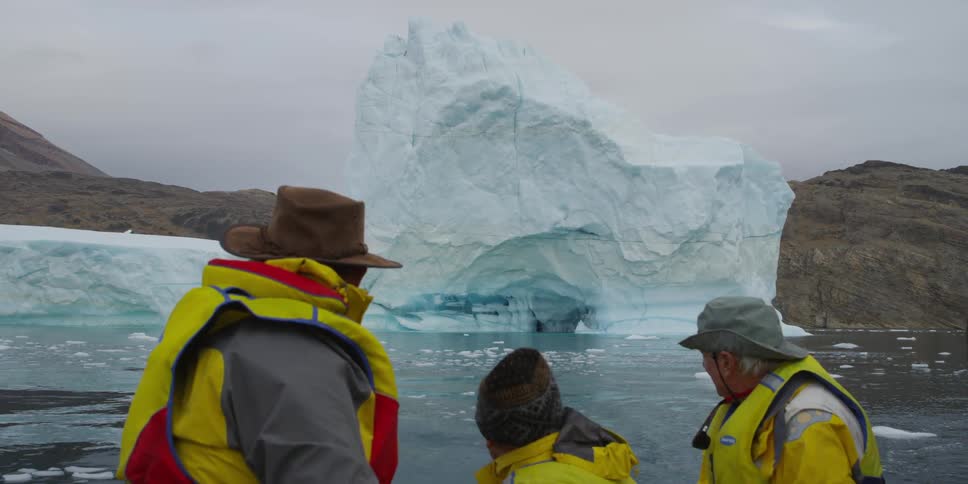 Three men sit on a boat near a glacier