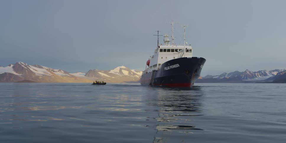 A ship floats on a body of water with a raft trailing behind