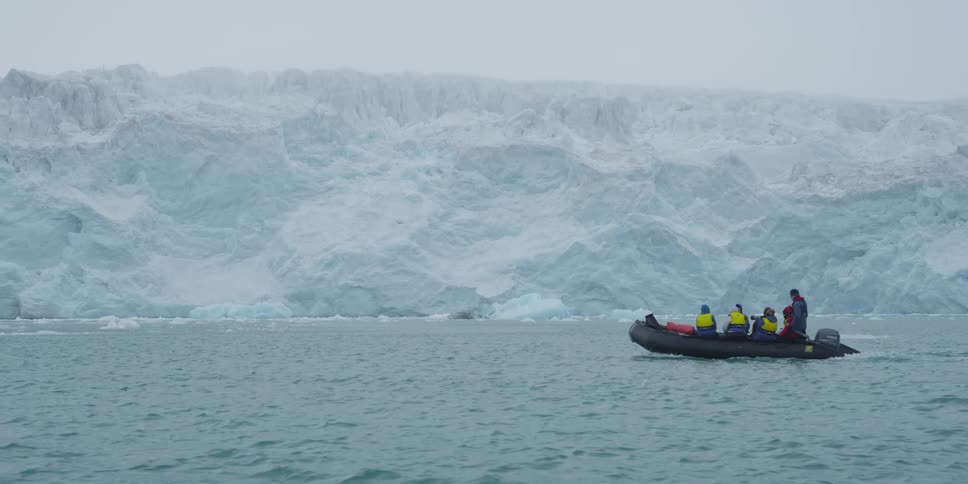 People are looking at a glacier while on a inflatable boat