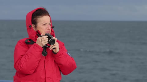 A woman takes a picture near the ocean on a windy day