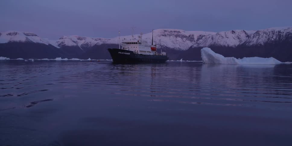 A ship's sits in a lake surrounded by icebergs and snow-capped mountains at dawn