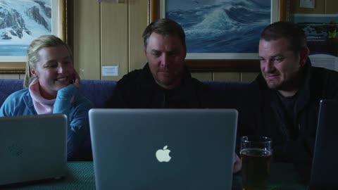A group of people sitting watching a laptop