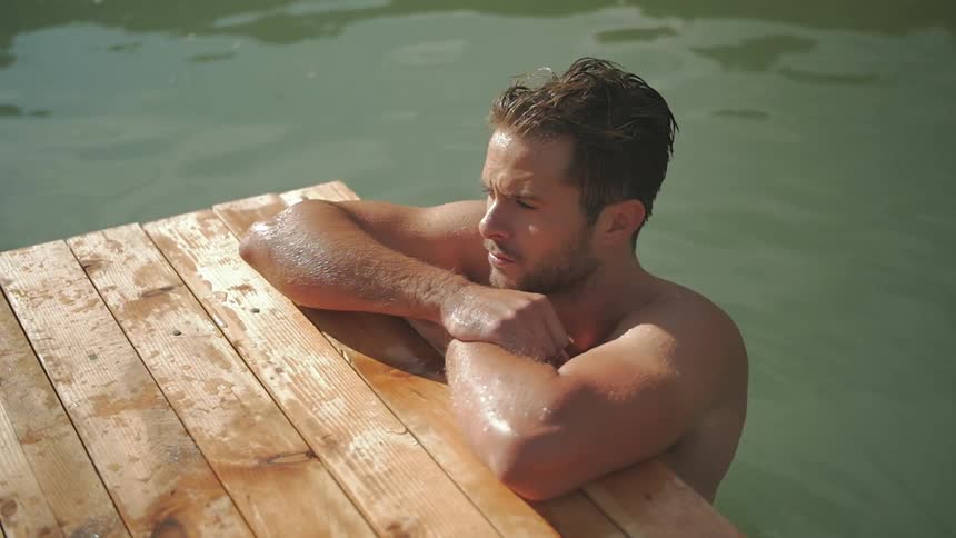 A man in a lake leans the end of a pier