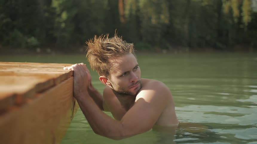 A man holds onto a dock while he swims in a lake