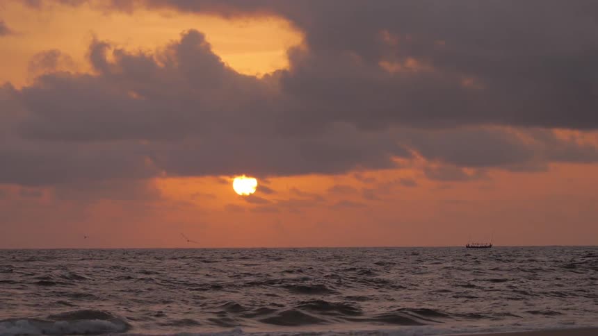 A ship floats on the ocean while the sun sets in the background