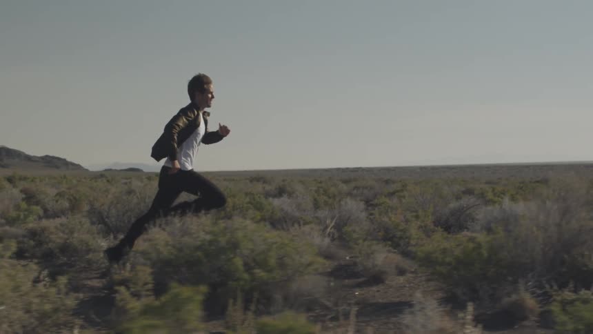 A man runs through a scrubby field in slow motion