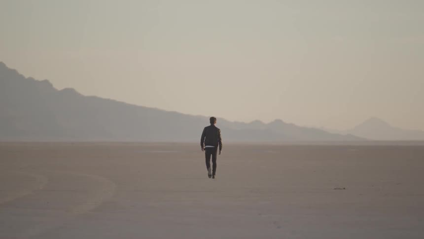 A man walking through an arid landscape towards mountains