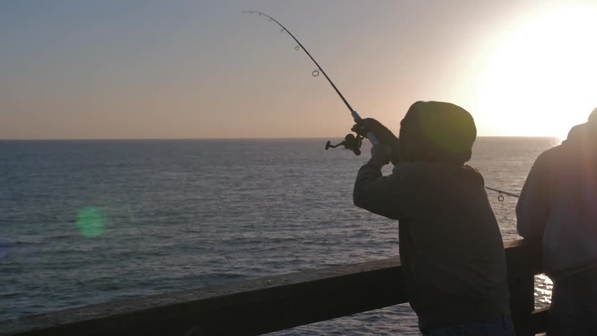 A person fishes at dusk from a pier
