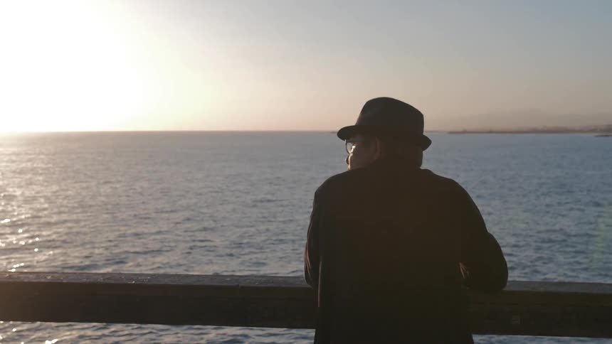 A man looks over the side of a boat during sunset