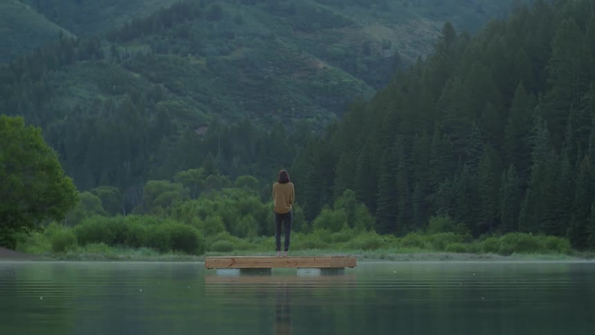 A person stands on a dock in the middle of a lake