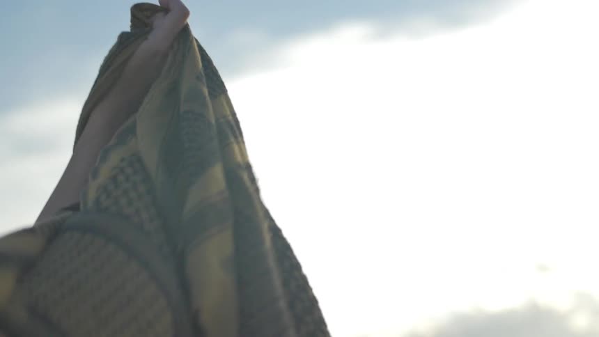 A person holds a scarf in the air so the wind can blow it