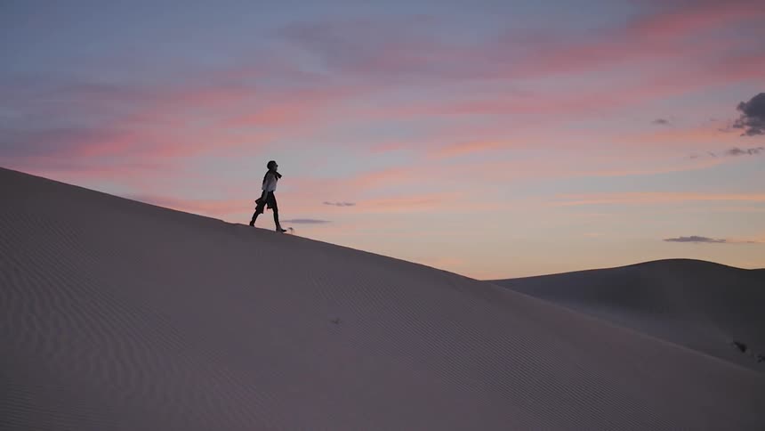 A woman walks down a sand dune at dusk