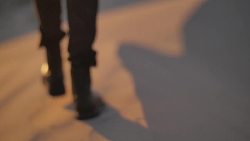 A person in boots walks through a sandy desert