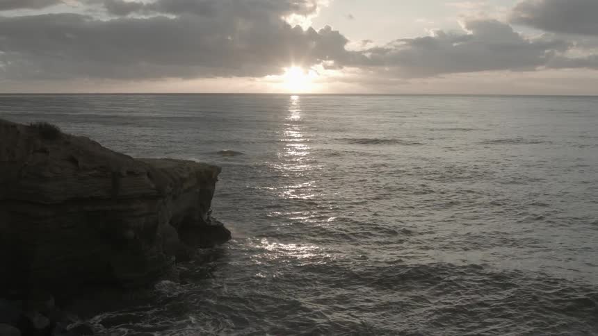 The sun falls beneath the clouds, while reflecting on the water