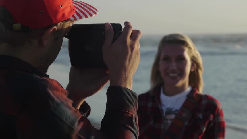 Man photographing a woman by the beach during the day