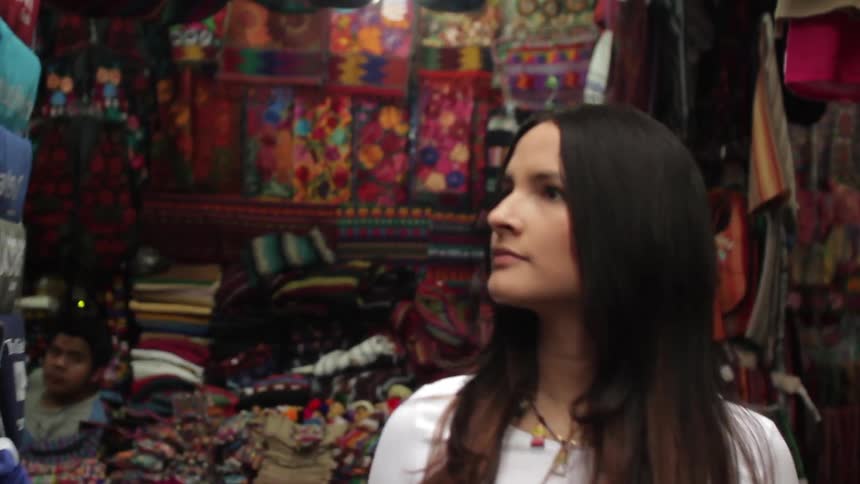 A young woman walks through market stalls filled with brightly colored clothes and knick knacks
