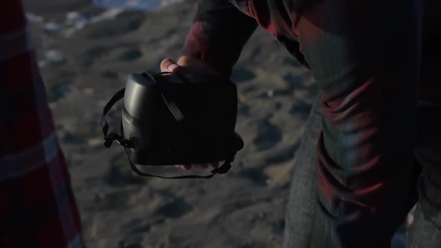 A man on the beach pulls a set of binoculars from a bag