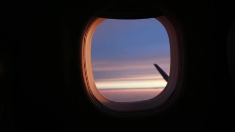 A passenger lifts the covering of an airplane window at sunset