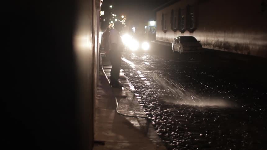 A man sprays water onto a street at night